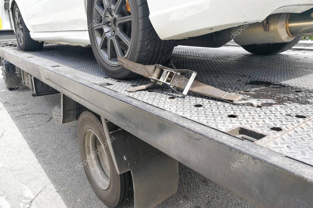 Car tire secured with safety belt on flatbed tow truck 