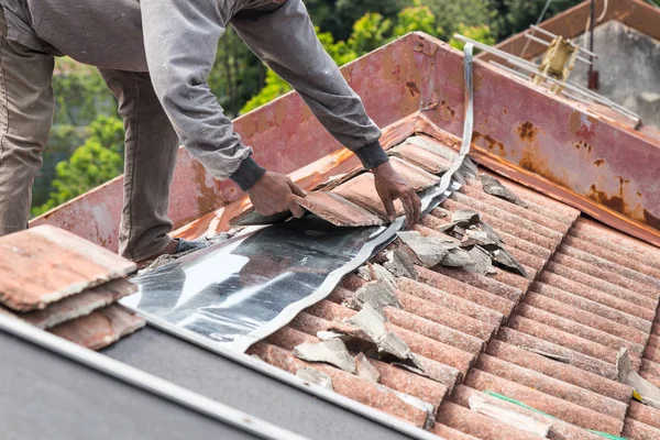Asian worker replacing roof tiles of old residential building