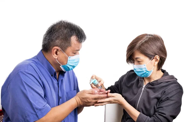 Femme asiatique avec masque facial appliquant un désinfectant sur la main de l'homme asiatique mature — Photo