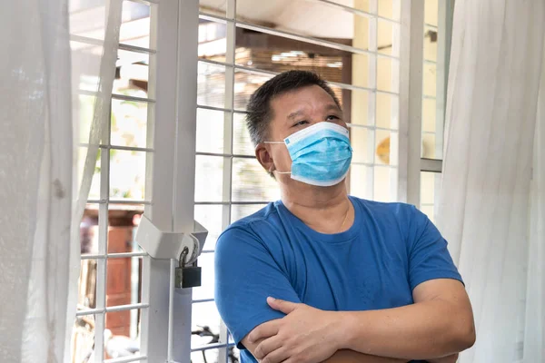 Anxious Chinese man with face mask self isolate quarantine at home for 14 days for fear of contact covid-19 virus