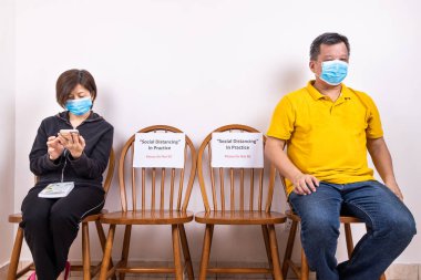Yüz maskesi olan kişiler, sosyal uzaklık ile halka açık bir yerde iki sandalye arasında oturan, Covid-19 salgınının yayılmasını önlemek için tabela oturma