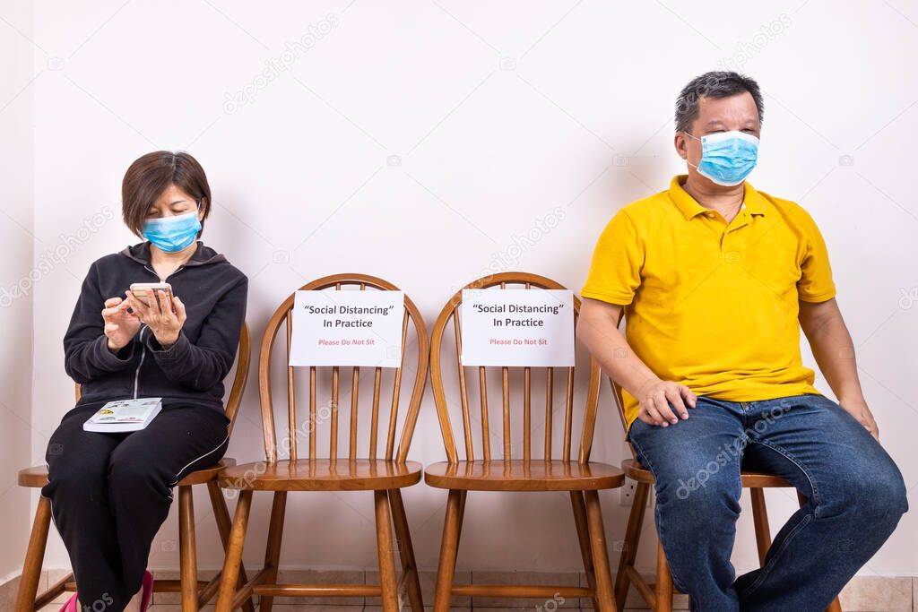 People with face mask seated in-between two chairs at public place, with Social Distancing, Do Not Sit signage to prevent spread of Covid-19 pandemic