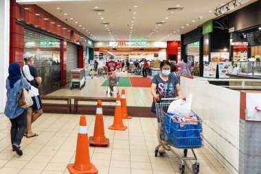 KUALA LUMPUR, MALAYSIA, 22 Mart 2020: Malezya 'da koronavirüs salgını olduğu gözlemlenen süpermarkete girmek için kuyruk oluşturan yüz maskeli müşteriler
