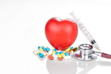 İlaç hapları, kaplet, tablet, kapsül ve kırmızı kalp, steteskop ve beyaz arka planda bir aksesuar olarak şırınga ile sağlık hizmeti kavramı