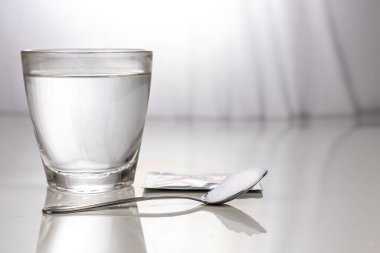 ORS or oral rehydration salt with glass of water, sachet and spoon on table against window light clipart