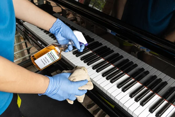Person in gloves disinfecting piano keyboard surface with disinfectant spray to kill germs, bacteria and virus.