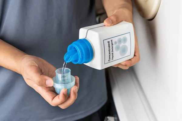 Person pouring concentrated liquid laundry detergent into measurement cap for washing