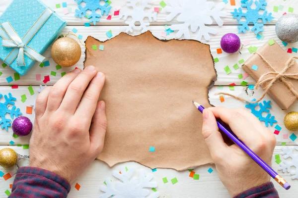 Homem escreve em uma lista de desejos no fundo de brinquedos de Natal e presentes — Fotografia de Stock