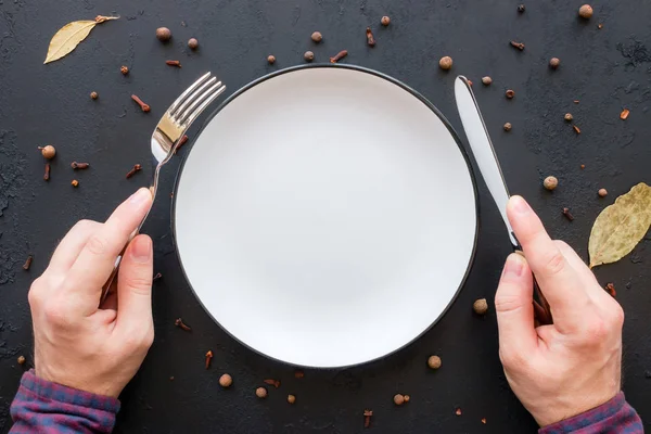 Man holding cutlery on a plate on a black background — Stock Photo, Image