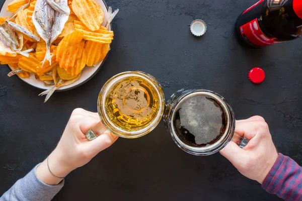 Menschen halten Becher mit dunklem und hellem Bier auf dem Hintergrund von Snacks mit Chips und Fisch — Stockfoto