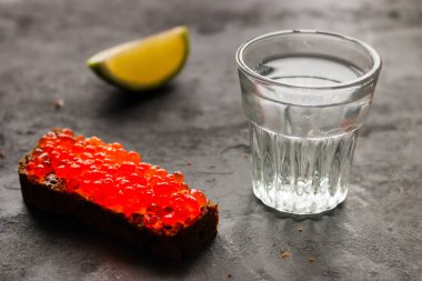 kadeh votka, kireç ve bir sandviç siyah bir zemin üzerine kırmızı havyar ile