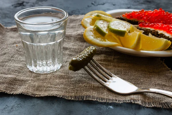 Sebuah piring dengan makanan ringan, segelas vodka dan gherkin pada garpu — Stok Foto