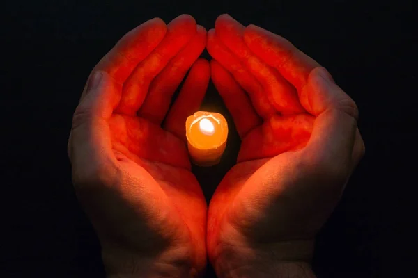 Due mani tengono una candela al buio. preghiera . — Foto Stock