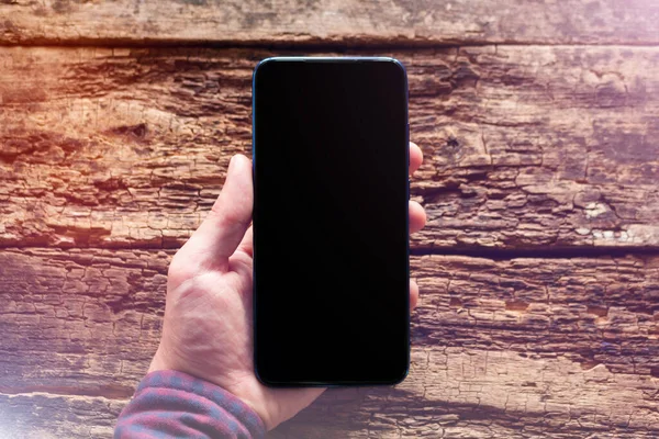 男は携帯電話を持っているテキストモックアップのための場所と木製の背景に空白の黒い画面を持つ — ストック写真