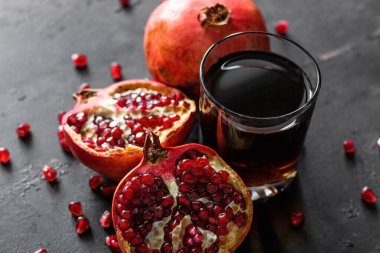 olgun nar meyvesi ve siyah arkaplanda meyve suyu olan bir bardak.