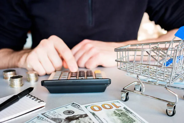 man counts money balance after taxes near shopping cart business purchase concept
