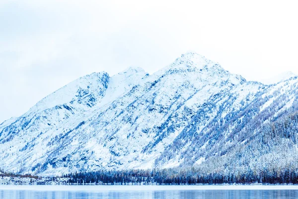 Winter lake with snow-covered pines on the Bank of the rocky mountains. The Altai mountains, fog over the winter lake.