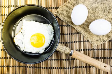 Bir tavada kızarmış yumurta ve ahşap bir masa üzerinde iki çiğ yumurta. Ev yapımı, rustik gıda.