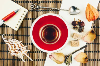 Kırmızı bir fincan çay ve bir ahşap masa üzerinde gül tomurcukları ile natürmort