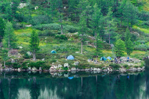 Tourist tents on the shore of a mountain lake. The camp of tourists on the water.