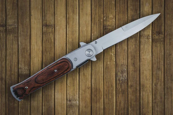 Folding combat knife on a wooden table. Instrument of crime
