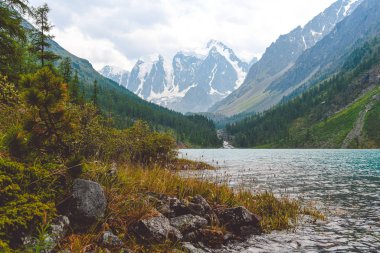 Vadinin ufuklarındaki karlı dağ zirveleri bulutların altında, dağlık alana seyahat eder.