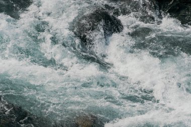 Güçlü dağ nehri. Kayalar arasında hızlı akış. Mavi su akıntısı kayalarda kaynıyor.
