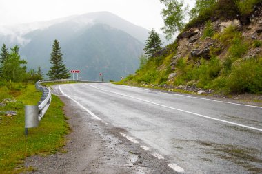 Dağ vadisindeki asfalt yolda ufukta kayalar var. Vahşi doğada arabayla rahat bir yolculuk.