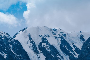 Bulutlu gökyüzünün altındaki dağ sırası. Dağların karlı zirveleri