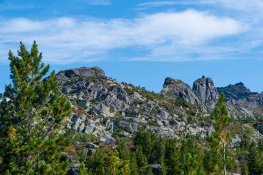 Dağ vadisinde mavi gökyüzünün altındaki kayalık sırt, dik yamaçlardaki tırmanışçıların yolculuğu.