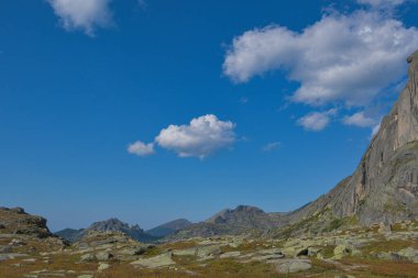 Mavi gökyüzünün altında bulutlar, kaya sırtına tırmanma hazırlığı, dağ vadisinde yolculuk