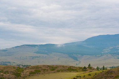 Ufuktaki kar zirveleri, dağ vadisindeki bulutlu gökyüzünün altındaki kayalıklar.