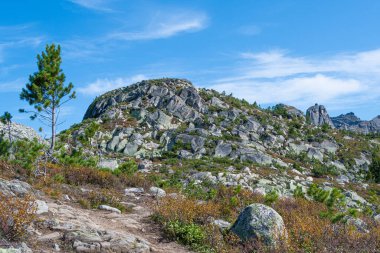 Dağ vadisinde mavi gökyüzünün altındaki kayalık sırt, dik yamaçlardaki tırmanışçıların yolculuğu.
