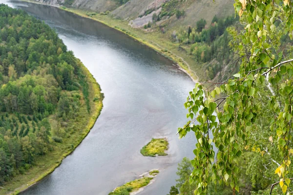 wide river among green hills with trees, smooth bend of channel, forest on shore of reservoir, summer swimming and navigation