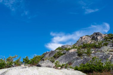 Dağ vadisinde mavi gökyüzünün altındaki kayalık sırt, dik yamaçlardaki tırmanışçıların yolculuğu.