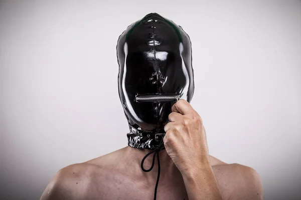 portrait of man closing zipper of his shiny latex mask