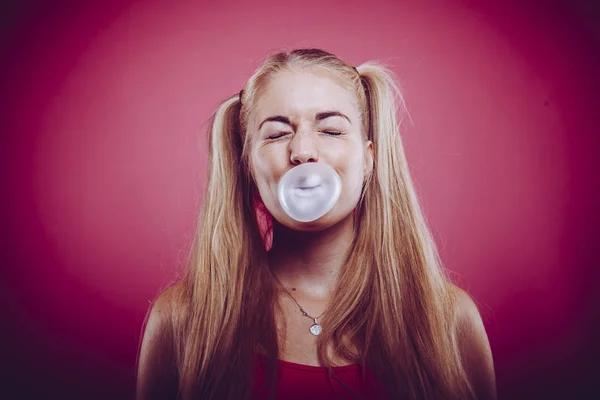 portrait of an anxious blonde woman blowing up chewing gum bubble afraid of bursting and sticking to her face