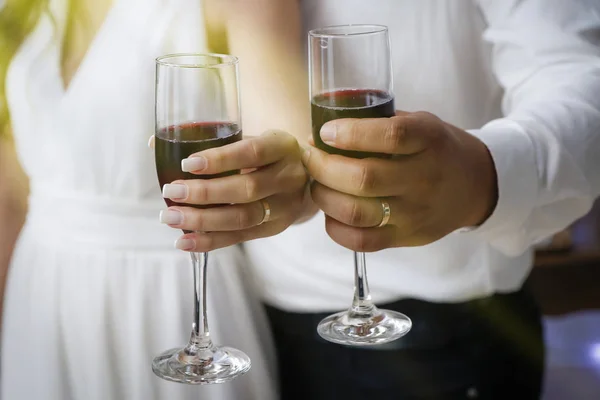 hands with wedding rings holding wine glasses