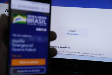Minas Gerais, MG / Brazil - 22 Nisan 2020: Brezilya Hükümeti acil yardım sayfası ile bilgisayar ekranı ve cep telefonu.