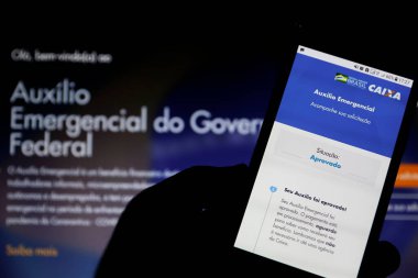 Minas Gerais / Brezilya - 26 Nisan 2020: Brezilya Hükümeti 'nin acil yardım sayfası ile bilgisayar ekranı ve cep telefonu, statü onayı.