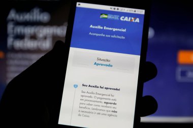 Minas Gerais / Brezilya - 26 Nisan 2020: Brezilya Hükümeti 'nin acil yardım sayfası ile bilgisayar ekranı ve cep telefonu, statü onayı.