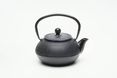 Beyaz zemin üzerinde siyah dökme demir çaydanlık.