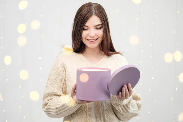 Young brunette woman in a sweater on a white background. Holding Christmas present box. Joy, happiness and surprise. — Stock Photo, Image