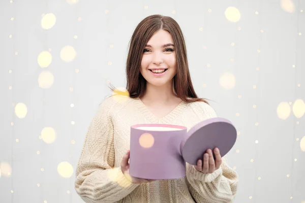 Joven morena en suéter sobre fondo blanco. La celebración de la caja de regalo de Navidad. Alegría, felicidad y sorpresa . —  Fotos de Stock