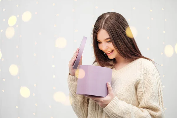 Jeune femme brune en pull sur fond blanc. Tenant une boîte cadeau de Noël. Joie, bonheur et surprise . — Photo