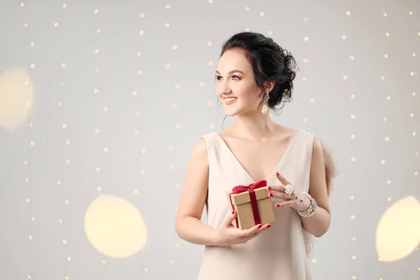 Mujer morena joven en vestido de noche sobre un fondo blanco. La celebración de la caja de regalo de Navidad. Alegría, felicidad y sorpresa . —  Fotos de Stock