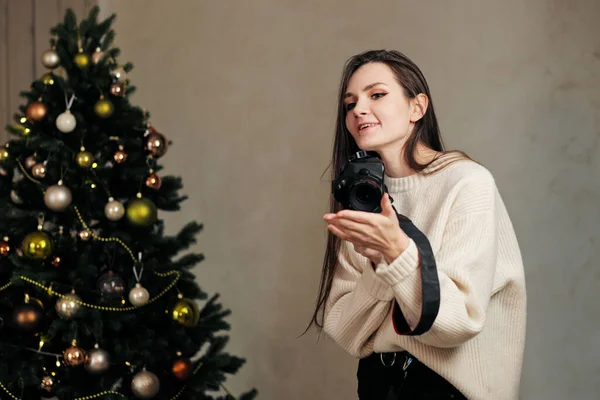 Jovem fotógrafa tira fotos em casa no fundo da árvore de Natal . — Fotografia de Stock