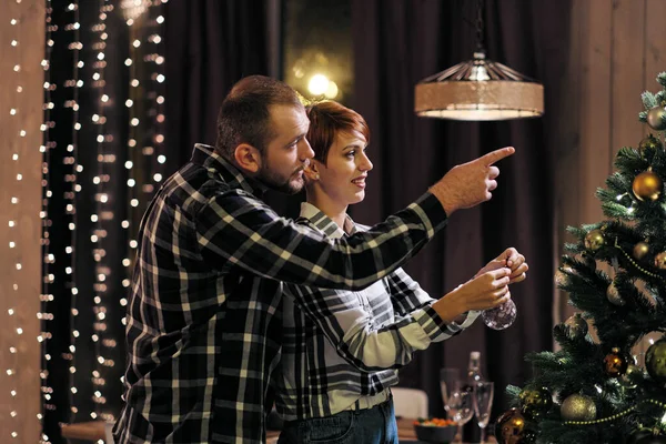 Jovem casal em casa em roupas casuais, um homem e uma mulher decorar a árvore de Natal . — Fotografia de Stock