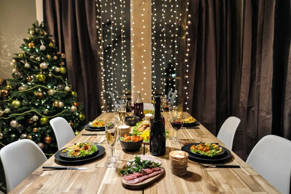 Feestelijke tafelschikking. Eten en drinken, borden en glazen. Avondlampjes en kaarsen. Oudejaarsavond. — Stockfoto