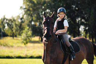 Genç kız jokey doğada kahverengi bir atın üzerinde oturuyor..